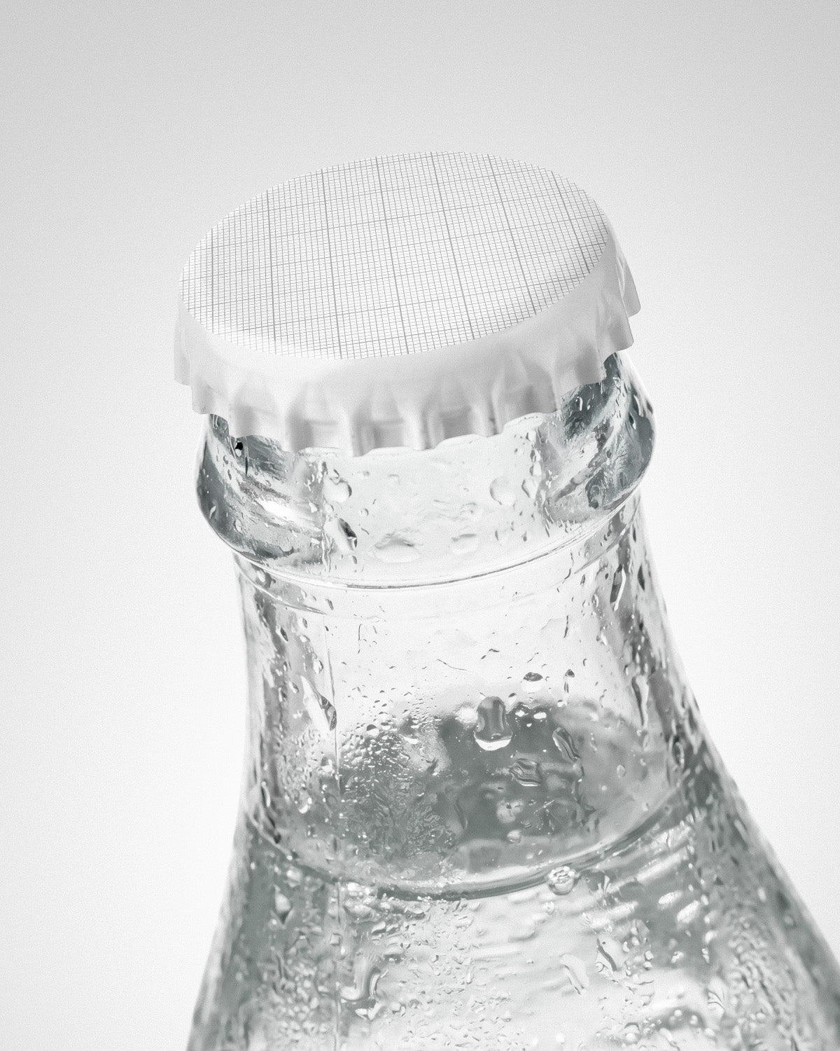 Glass bottle mockup with grid crown cap and clear water with condensation droplets