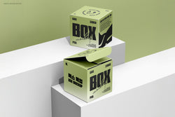 Two square boxes on minimalistic white blocks with a green background, one box open showing inner flap design.